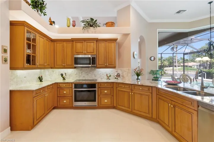Kitchen featuring stainless steel appliances, backsplash, a sink, light stone countertops, and brown cabinets