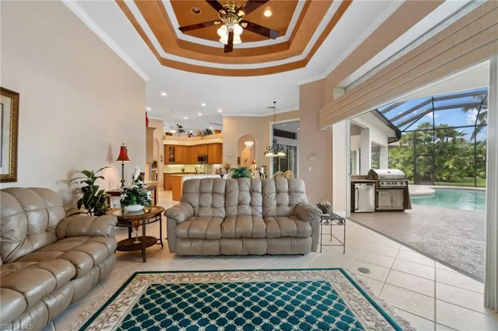 Living room featuring a tray ceiling, light tile patterned flooring, a ceiling fan, a towering ceiling, and ornamental molding