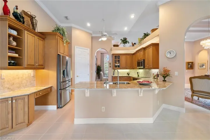 Kitchen featuring a sink, a peninsula, brown cabinetry, stainless steel appliances, and arched walkways