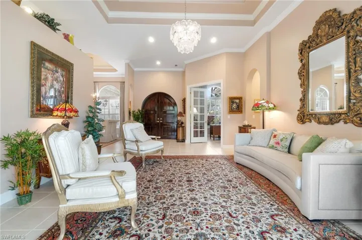 Tiled living area with a tray ceiling, recessed lighting, ornamental molding, baseboards, and a chandelier