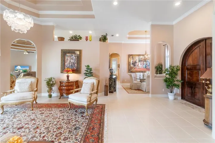 Foyer with a tray ceiling, crown molding, baseboards, a chandelier, and arched walkways