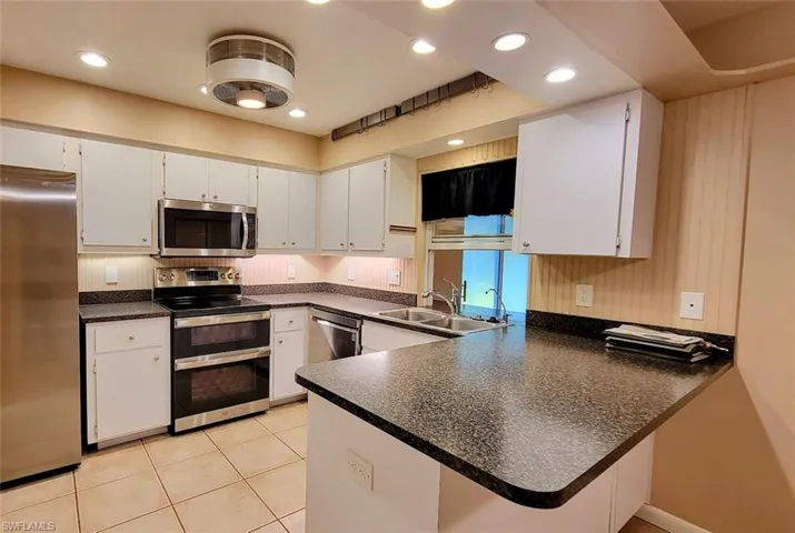 Kitchen featuring stainless steel appliances, dark countertops, white cabinets, and a peninsula