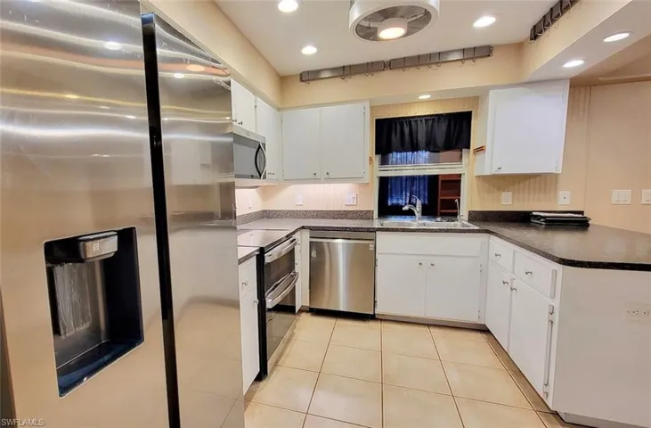 Kitchen with stainless steel appliances, dark countertops, white cabinets, a sink, and a peninsula