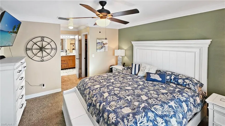 Bedroom featuring crown molding, baseboards, light carpet, ensuite bath, and a ceiling fan