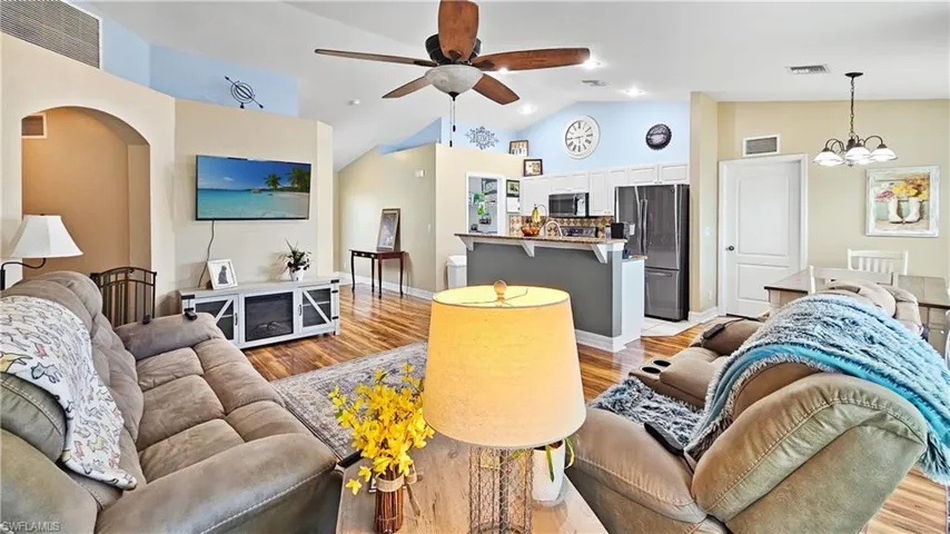 Living room with light wood-type flooring, visible vents, and ceiling fan with notable chandelier