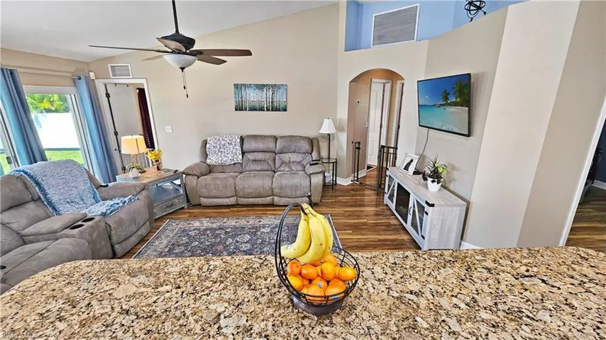 Living area with a ceiling fan, wood finished floors, arched walkways, and visible vents