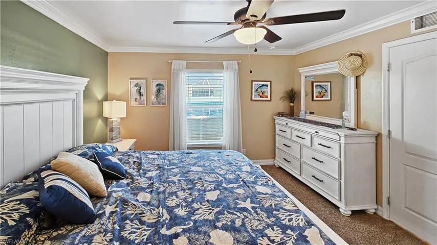 Bedroom with a ceiling fan, baseboards, visible vents, ornamental molding, and dark colored carpet