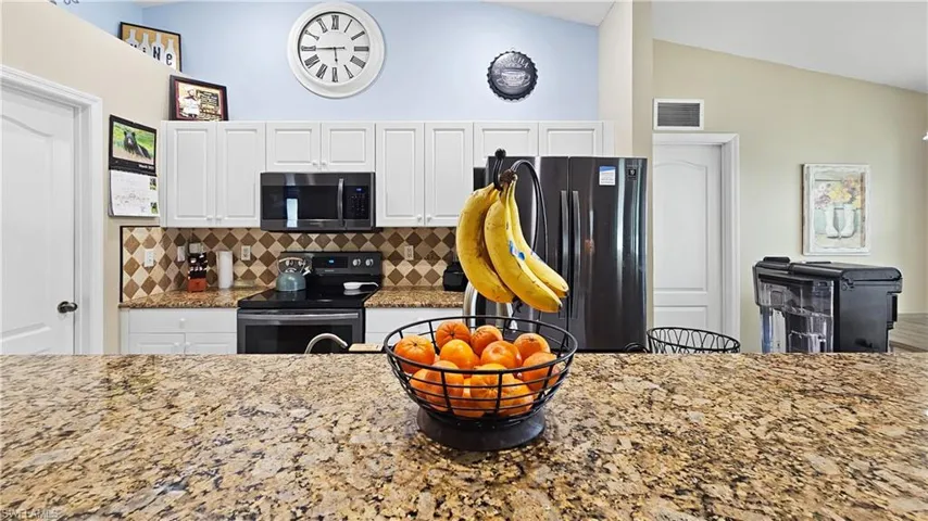Kitchen with visible vents, white cabinetry, appliances with stainless steel finishes, decorative backsplash, and vaulted ceiling