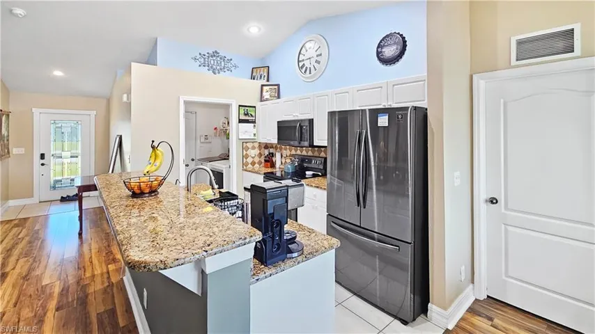 Kitchen featuring light stone counters, visible vents, decorative backsplash, white cabinets, and appliances with stainless steel finishes