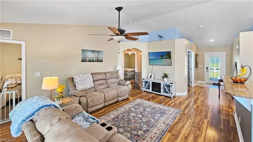 Living room with visible vents, vaulted ceiling, wood finished floors, arched walkways, and a ceiling fan