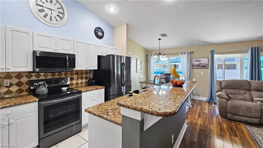 Kitchen with open floor plan, vaulted ceiling, dark stone countertops, range with electric stovetop, and freestanding refrigerator