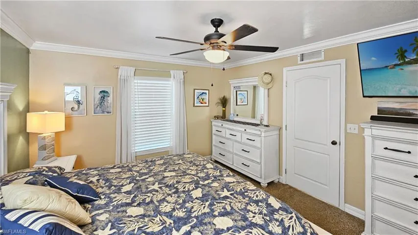 Carpeted bedroom with a ceiling fan, visible vents, and ornamental molding