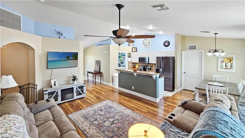 Living area with visible vents, arched walkways, light wood-style flooring, and ceiling fan with notable chandelier