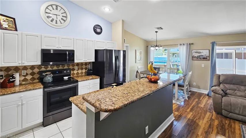 Kitchen with visible vents, lofted ceiling, electric range oven, stone counters, and freestanding refrigerator