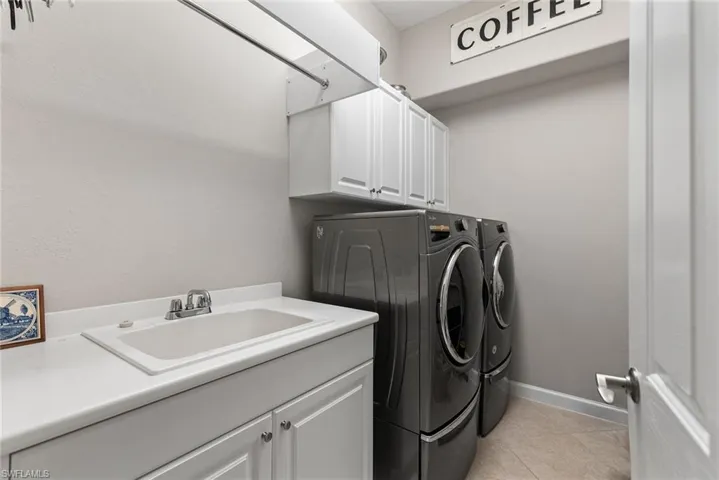 Laundry room featuring washer and clothes dryer, cabinet space, light tile patterned floors, and a textured wall