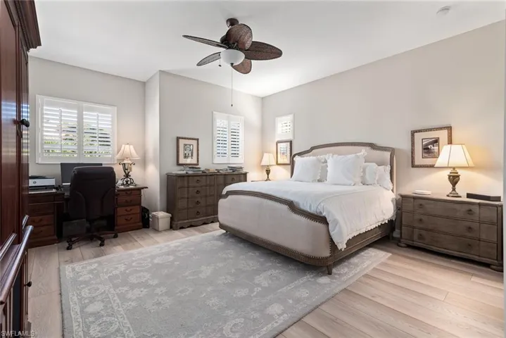 Bedroom featuring light wood-style flooring, a ceiling fan, multiple windows, and a desk