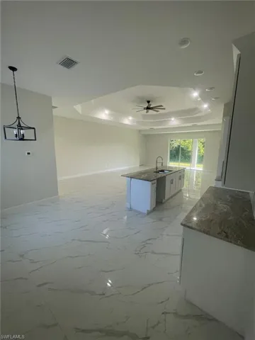 Tiled empty room featuring ceiling fan, sink, and a tray ceiling