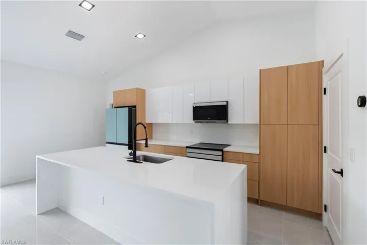 Kitchen with appliances with stainless steel finishes, a sink, high vaulted ceiling, a kitchen island with sink, and modern cabinets