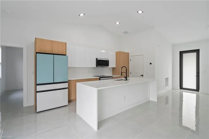 Kitchen with white fridge, stainless steel microwave, a center island with sink, light countertops, and light tile patterned flooring