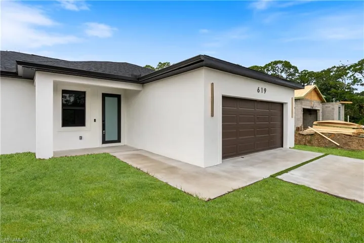 View of front of property featuring an attached garage, driveway, stucco siding, and a front lawn