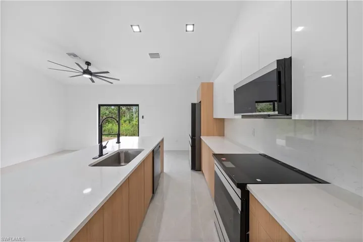 Kitchen featuring modern cabinets, black appliances, a sink, ceiling fan, and backsplash