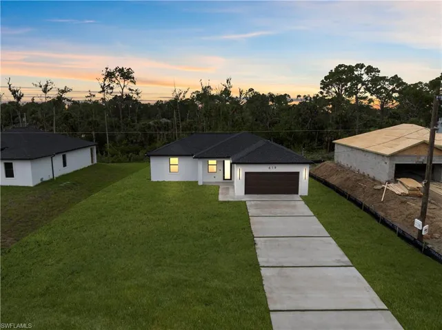 View of front facade featuring a front lawn, concrete driveway, a garage, stucco siding, and a shingled roof