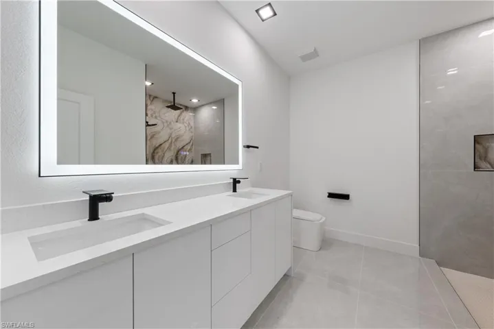 Full bathroom with a walk in shower, double vanity, toilet, marble look tiles, and baseboards