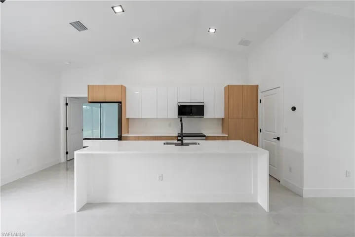 Kitchen featuring freestanding refrigerator, modern cabinets, an island with sink, white cabinets, and light countertops