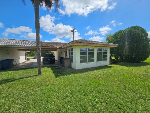 Rear view of property with a yard, stucco siding, an attached carport, and a patio
