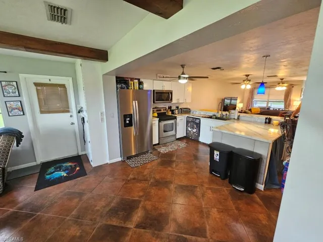 Kitchen with a peninsula, appliances with stainless steel finishes, open floor plan, white cabinets, and hanging light fixtures