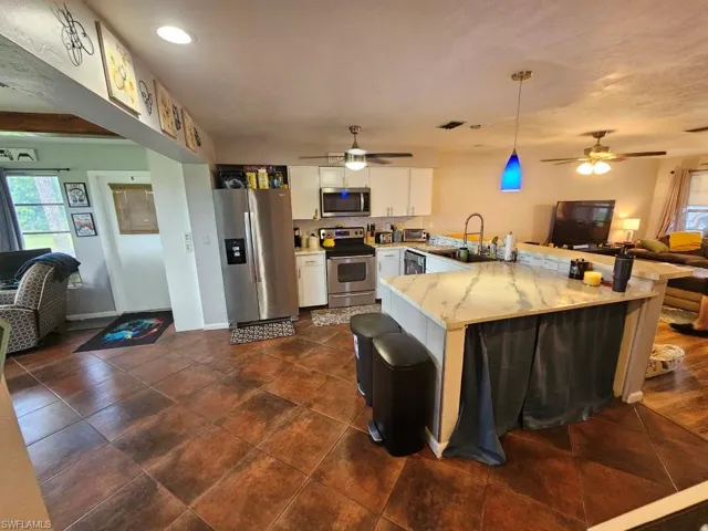Kitchen featuring open floor plan, a peninsula, stainless steel appliances, white cabinetry, and pendant lighting