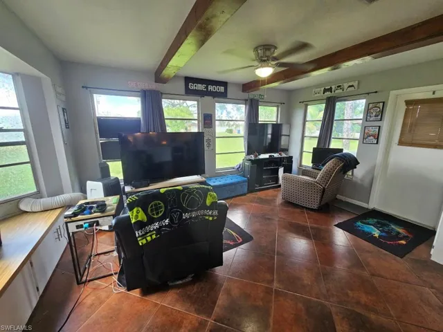 Living area featuring beamed ceiling, a ceiling fan, and dark tile patterned flooring