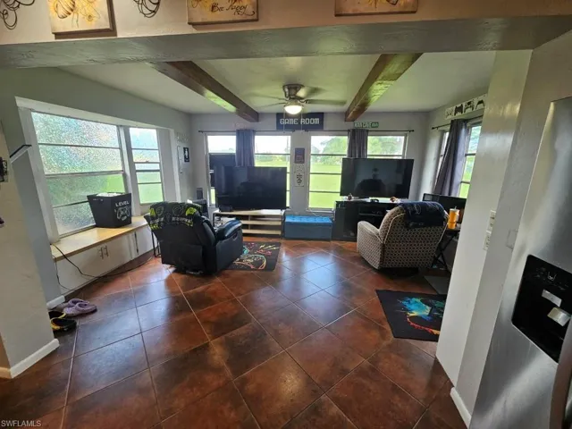 Living room featuring beam ceiling, dark tile patterned flooring, a textured wall, and ceiling fan