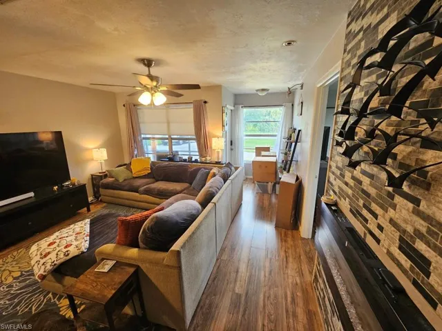 Living area with dark wood-type flooring, a textured ceiling, and ceiling fan