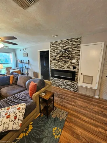 Living area with wood finished floors, a large fireplace, a textured ceiling, and ceiling fan