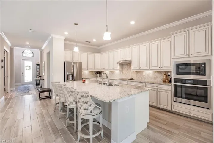 Kitchen featuring an island with sink, built in appliances, and light granite counters. Refriderator with Keurig coffee maker