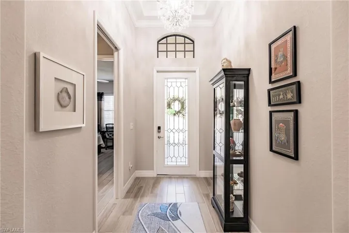 Entrance foyer with ornamental molding, light plank tile flooring, and a chandelier