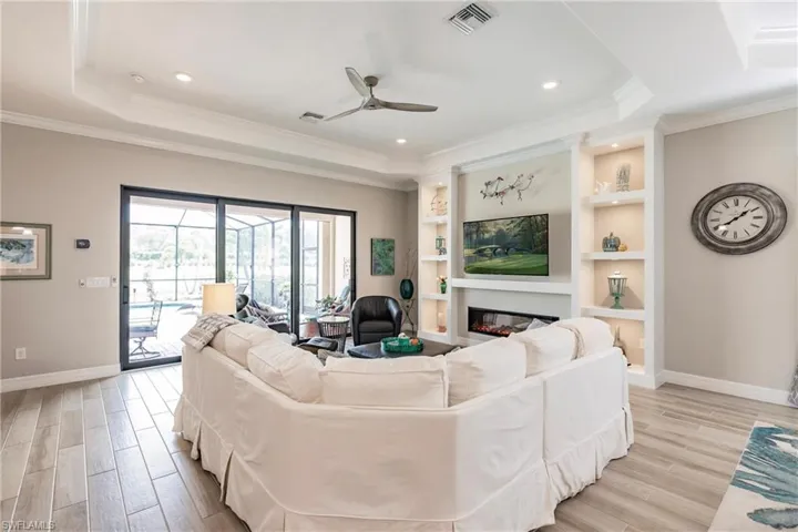 Living room with a raised ceiling, crown molding, ceiling fan and customized built in cabinets, including a linear fireplace.