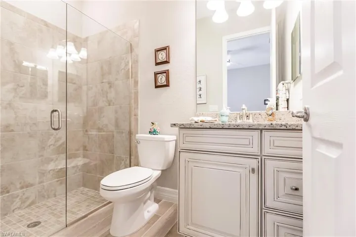 Ensuite guest bathroom featuring a tiled seamless door walk in shower, and vanity with granite countertop.