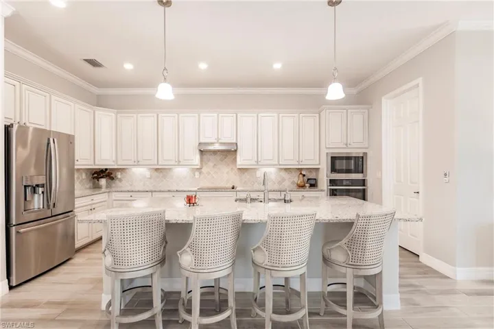 Kitchen with sink, stainless steel appliances, decorative light fixtures, white cabinets, and a kitchen island with sink