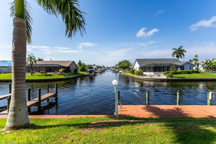 View of dock with glass enclosure, a lawn, and a water view