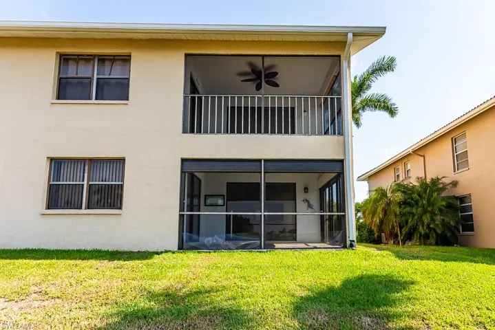 Back of house featuring ceiling fan, a yard, and a balcony
