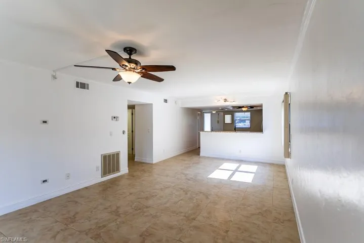 Unfurnished living room with ceiling fan, light tile patterned floors, and crown molding