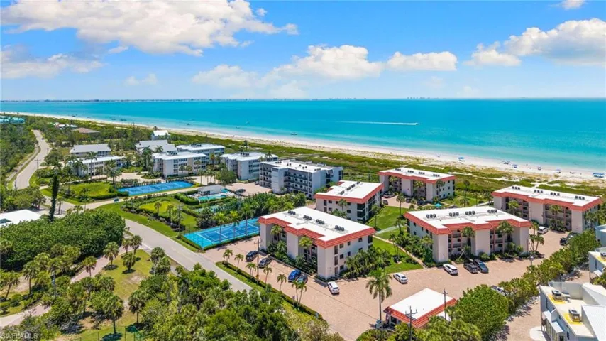 Coastal community featuring multiple residential buildings, direct beach access, tennis courts, and mature landscaping