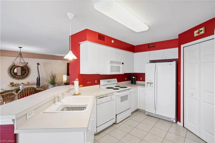 Kitchen featuring white appliances, white cabinets, pendant lighting, kitchen peninsula, and light tile patterned floors