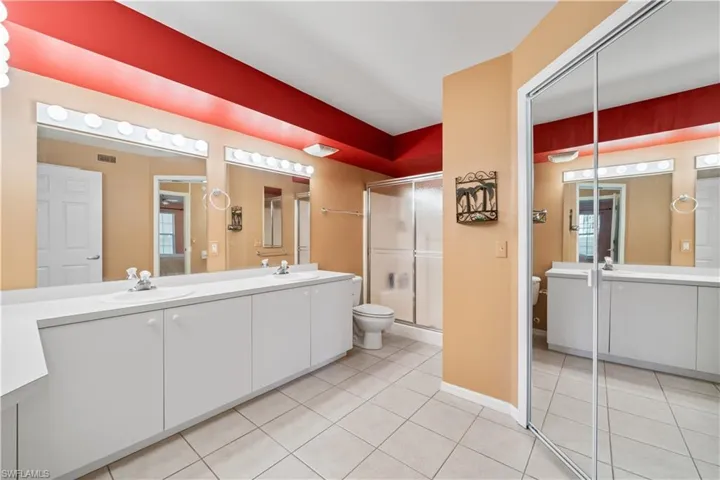 Bathroom featuring toilet, tile patterned floors, a walk in shower. dual vanities. Large walk in closet.