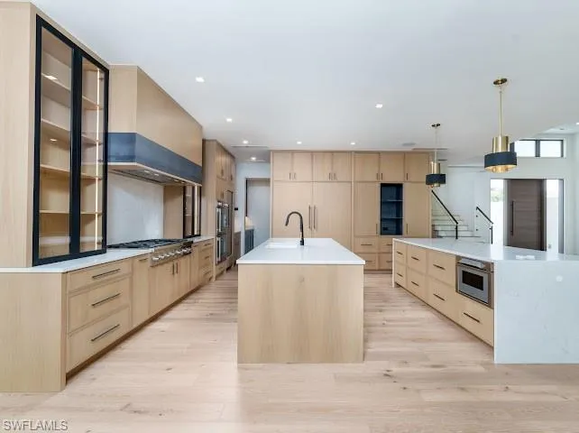 Kitchen with light wood finish cabinets, light stone counters, light wood finished floors, and decorative light fixtures