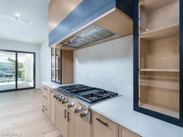 Kitchen with stainless steel gas cooktop, light stone counters, and light wood-style flooring