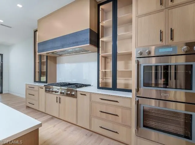 Kitchen featuring stainless steel appliances, light wood finish cabinetry, light wood-style floors, glass fronted cabinets, and recessed lighting