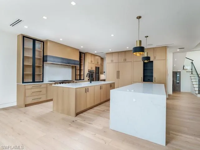 Kitchen with light wood finish cabinetry, light stone countertops, light wood-type flooring, and decorative light fixtures